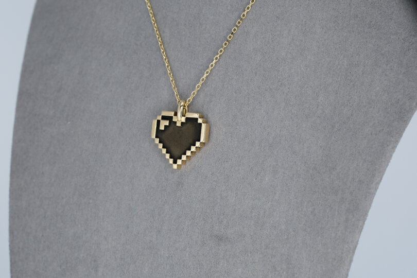 Gold heart-shaped pixel art pendant necklace displayed on a mannequin.