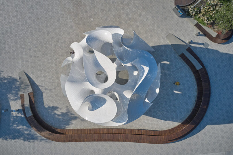 Aerial view showing the circular geometric layout and swirling shapes of the white sculpture on the plaza.