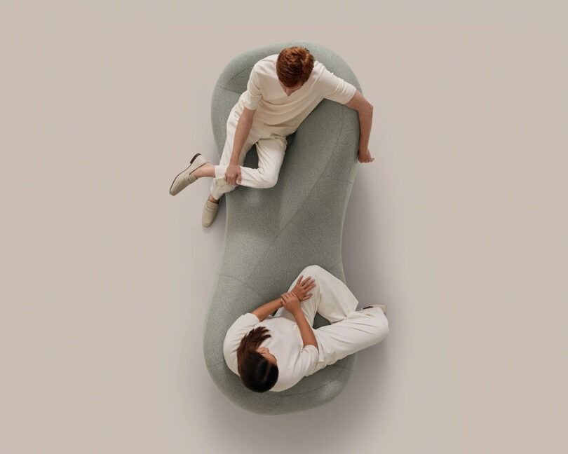 Aerial view of two people talking while sitting on a bean-shaped light gray sofa.