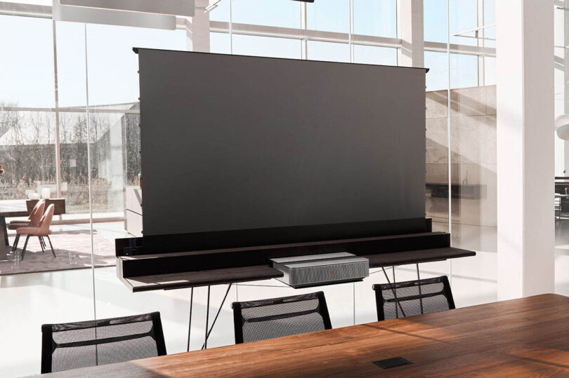 A modern conference room with a large retractable projection screen and a projector on the table.