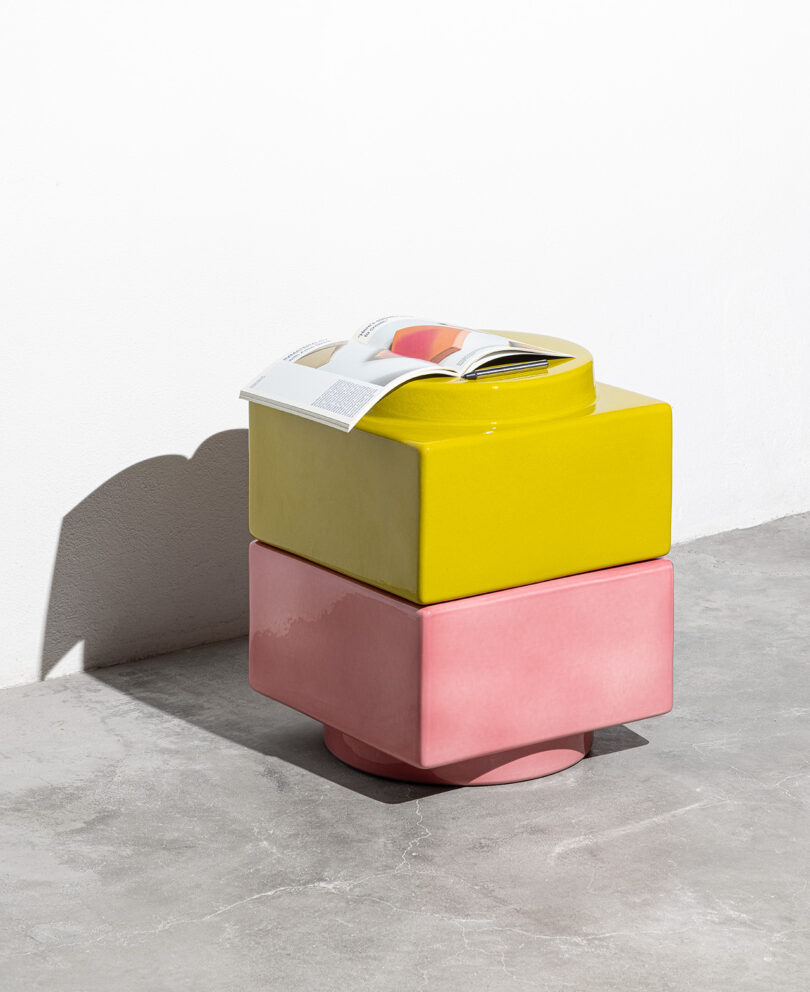 A magazine resting on top of a stacked pink and yellow ceramic unit in a minimalist room.