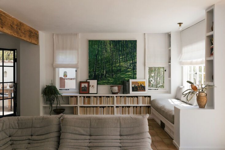 A plush window seat with oversized cushions nestled between floor-to-ceiling bookshelves in a Spanish-style villa.