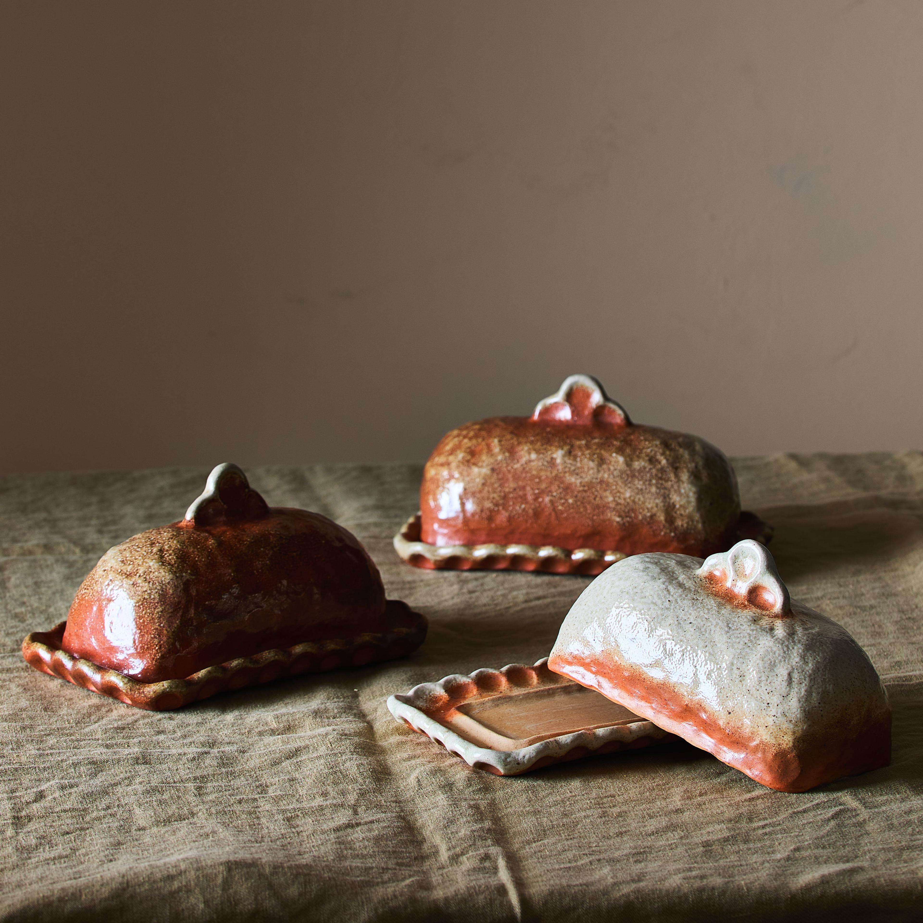 A wood-fired ceramic butter dish showing earthy brown and grey textures from natural ash melt.