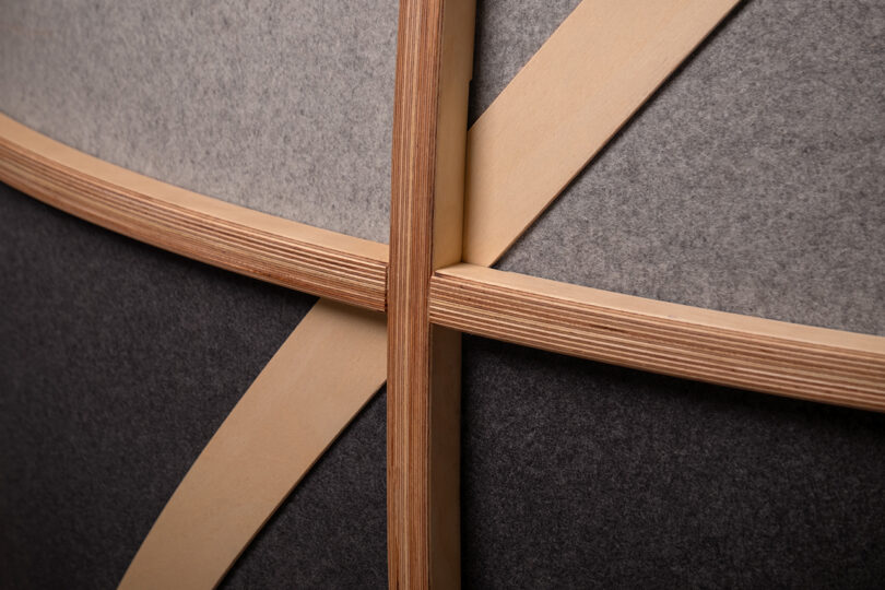 Close-up of intersecting light wood slats and textured grey sound-absorbing felt panels.