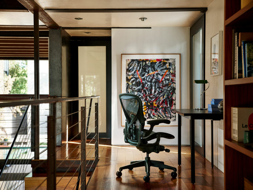 A black Aeron chair in a minimalist home office with wooden floors and an abstract painting.