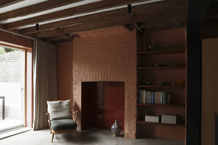 An earthy-pink kitchen with glossy red tiles and a vintage Ercol lounge chair.