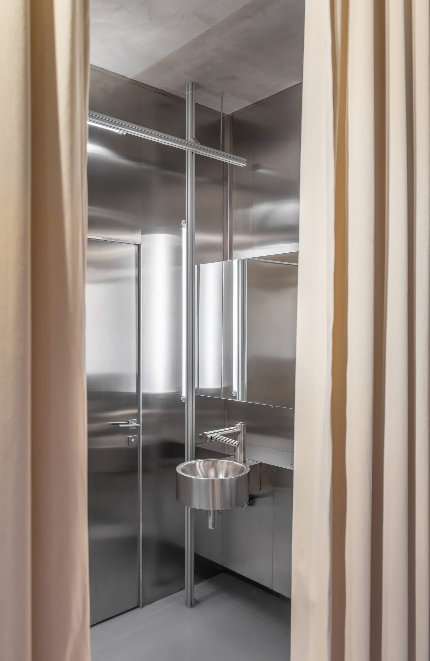 Close-up of the textural contrast between raw concrete walls and polished stainless steel fixtures.