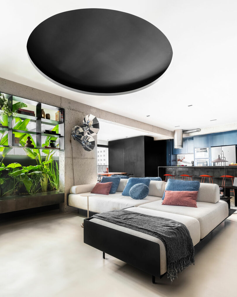 Open-concept living area with a white sectional sofa, large circular ceiling fixture, and integrated kitchen.