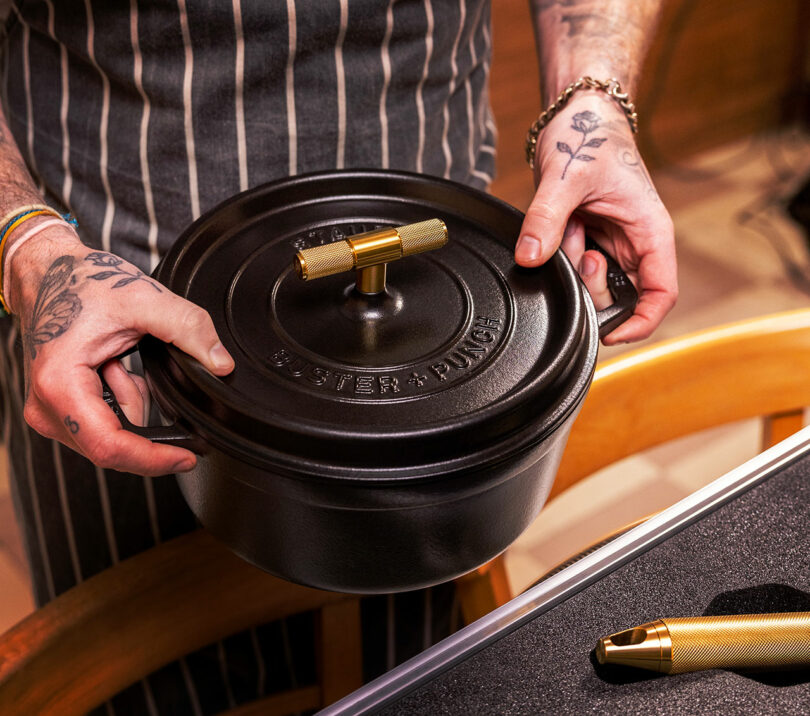 A person holding a black Staub cast iron pot with 'BUSTER + PUNCH' engraved on the lid.