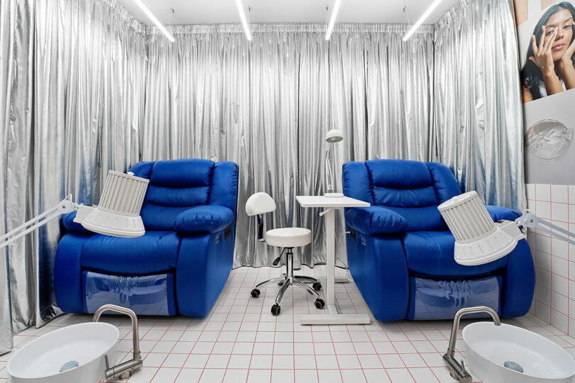 Two cobalt blue reclining chairs for pedicures surrounded by reflective silver metallic curtains.