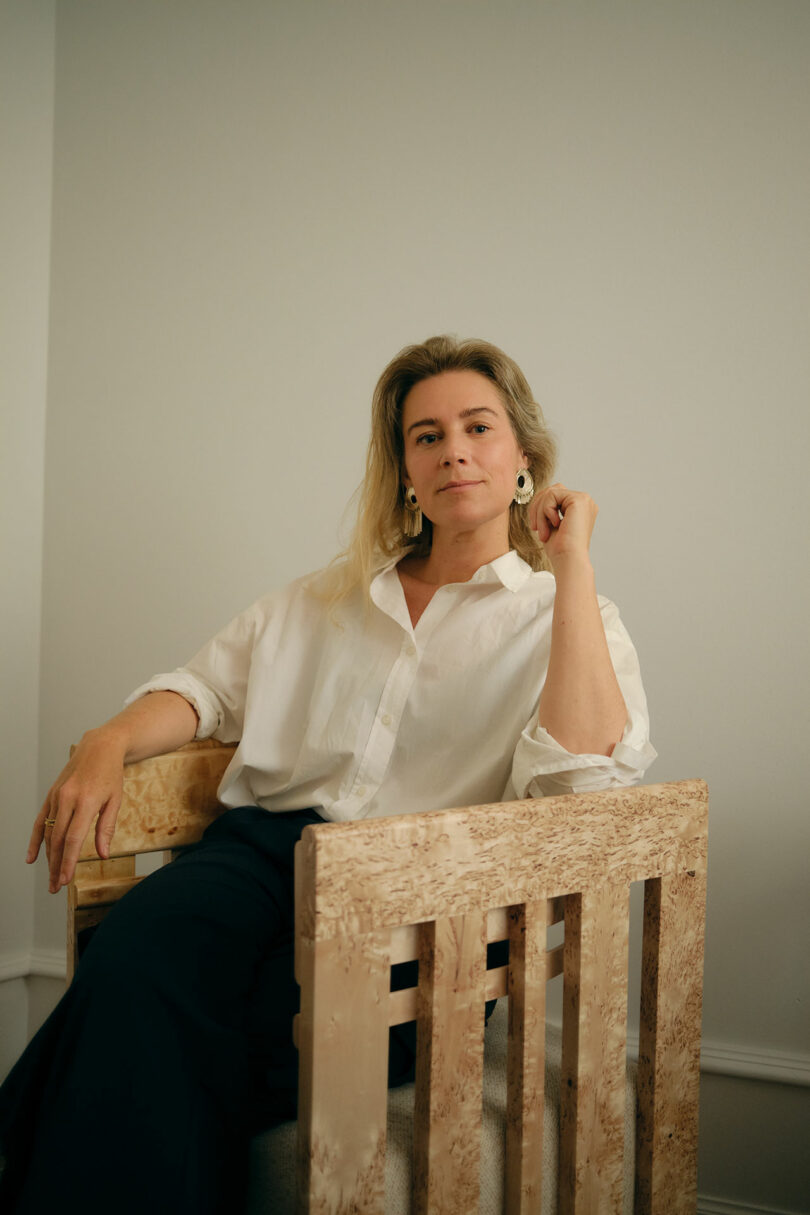 Portrait of designer Maria Bruun sitting in a wooden chair against a neutral background.