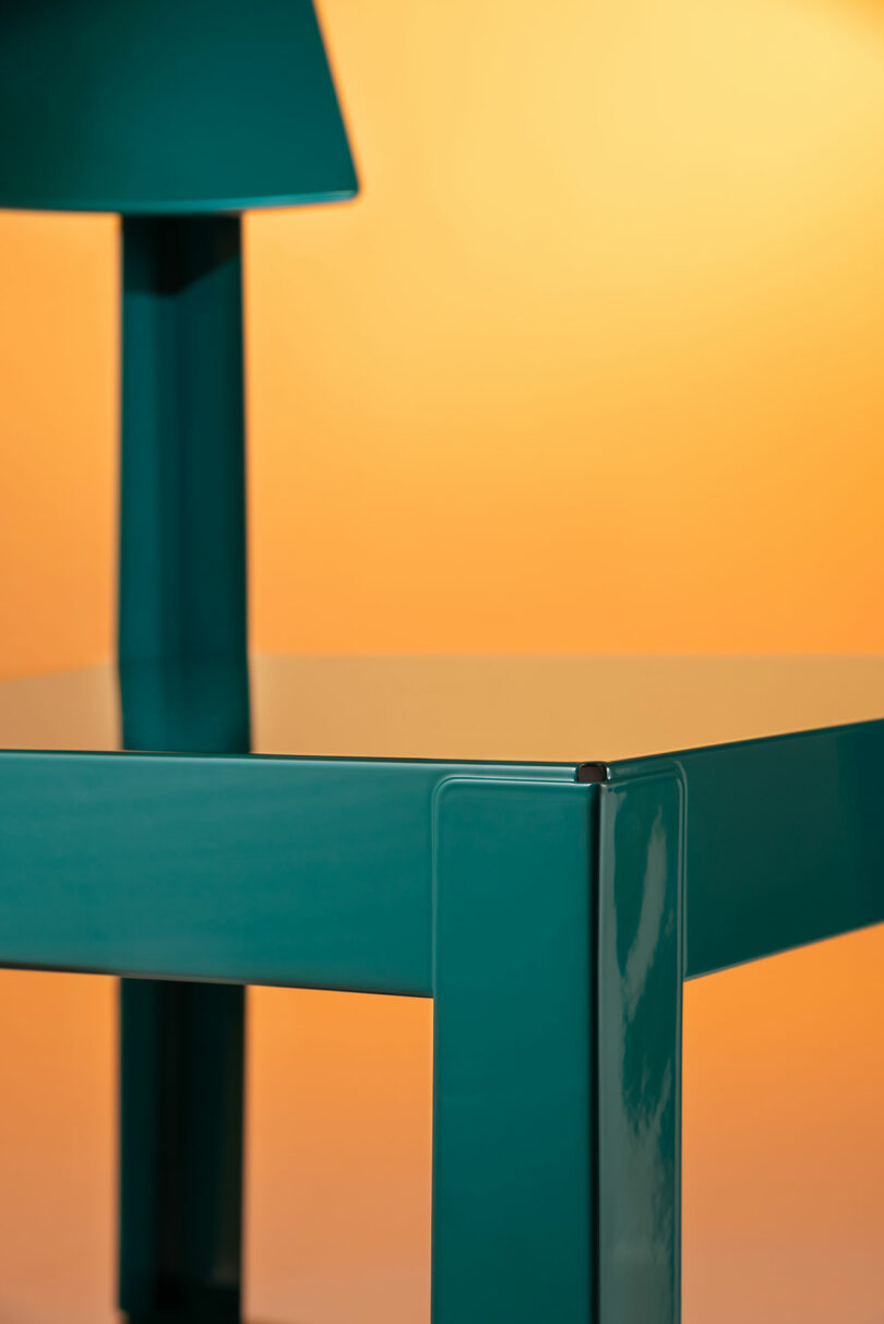 Close-up of a glossy teal metal chair seat and legs against an orange background.