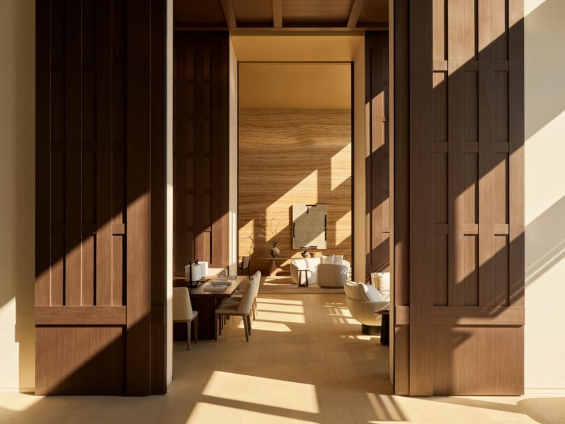 A serene room with large wooden doors, warm sunlight, and textured walls showcasing high-end craftsmanship.
