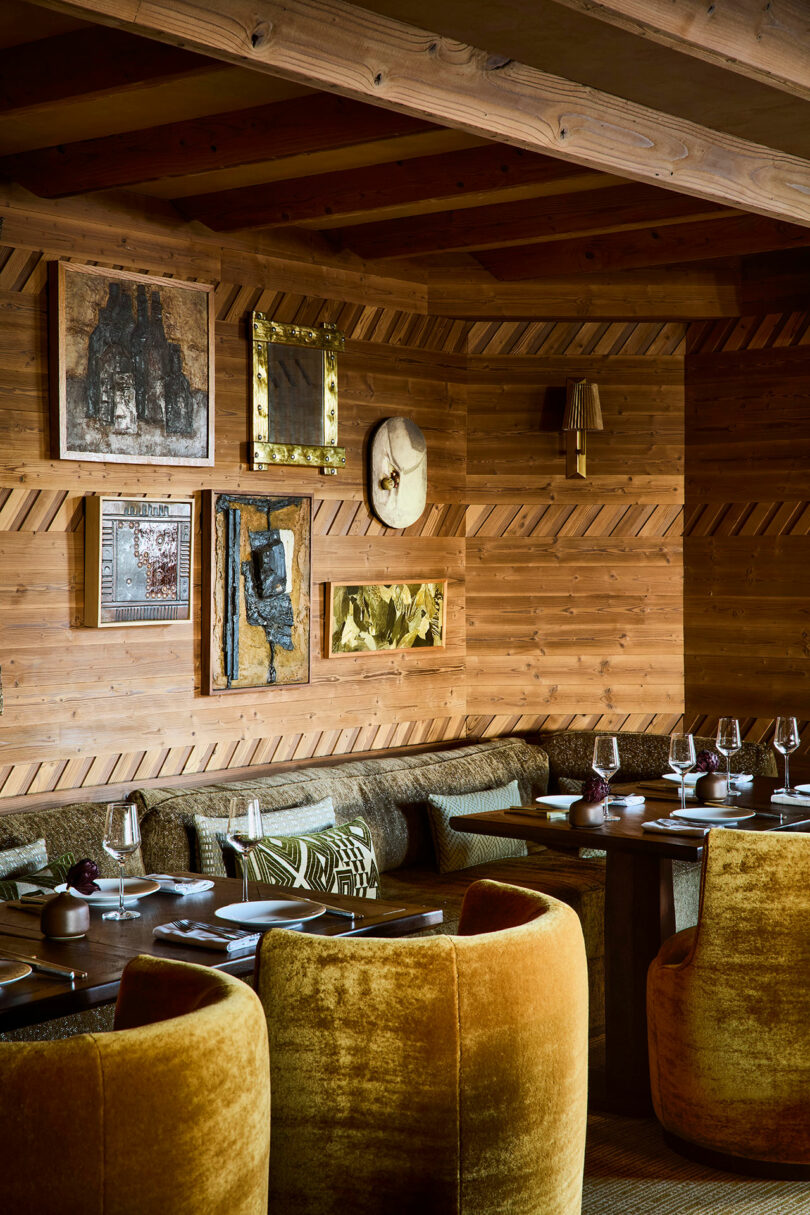 A restaurant interior with mustard yellow velvet chairs and wood-paneled walls decorated with framed art.