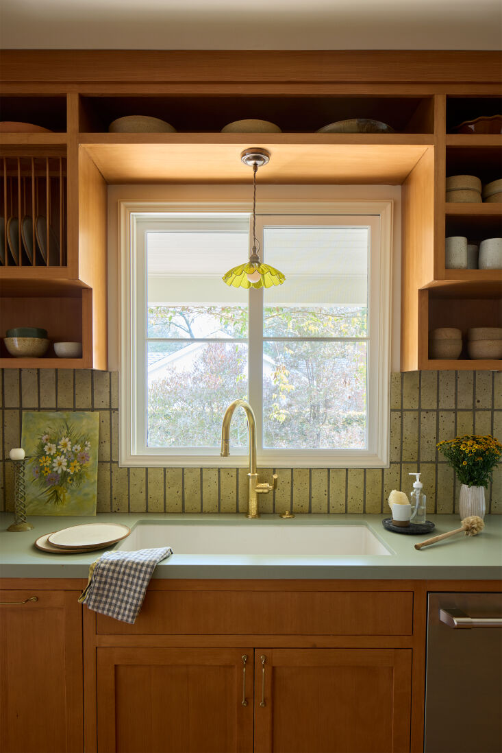A kitchen sink area with a green pendant light and brass fixtures.