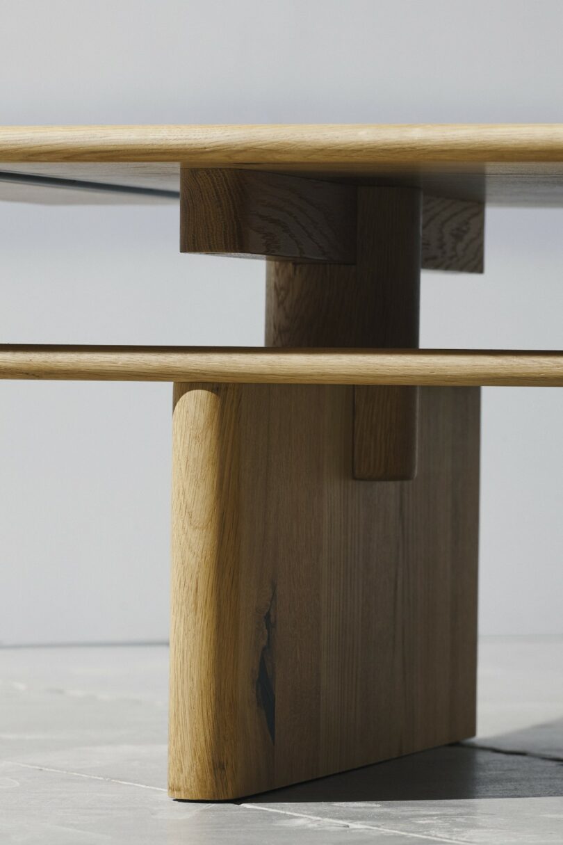 Close-up of a modern wooden table showing geometric vertical supports and natural wood finish.