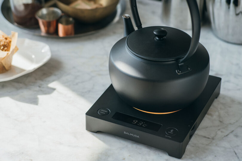 A black BALMUDA MoonKettle resting on a base displaying a digital temperature of 93 degrees Celsius.