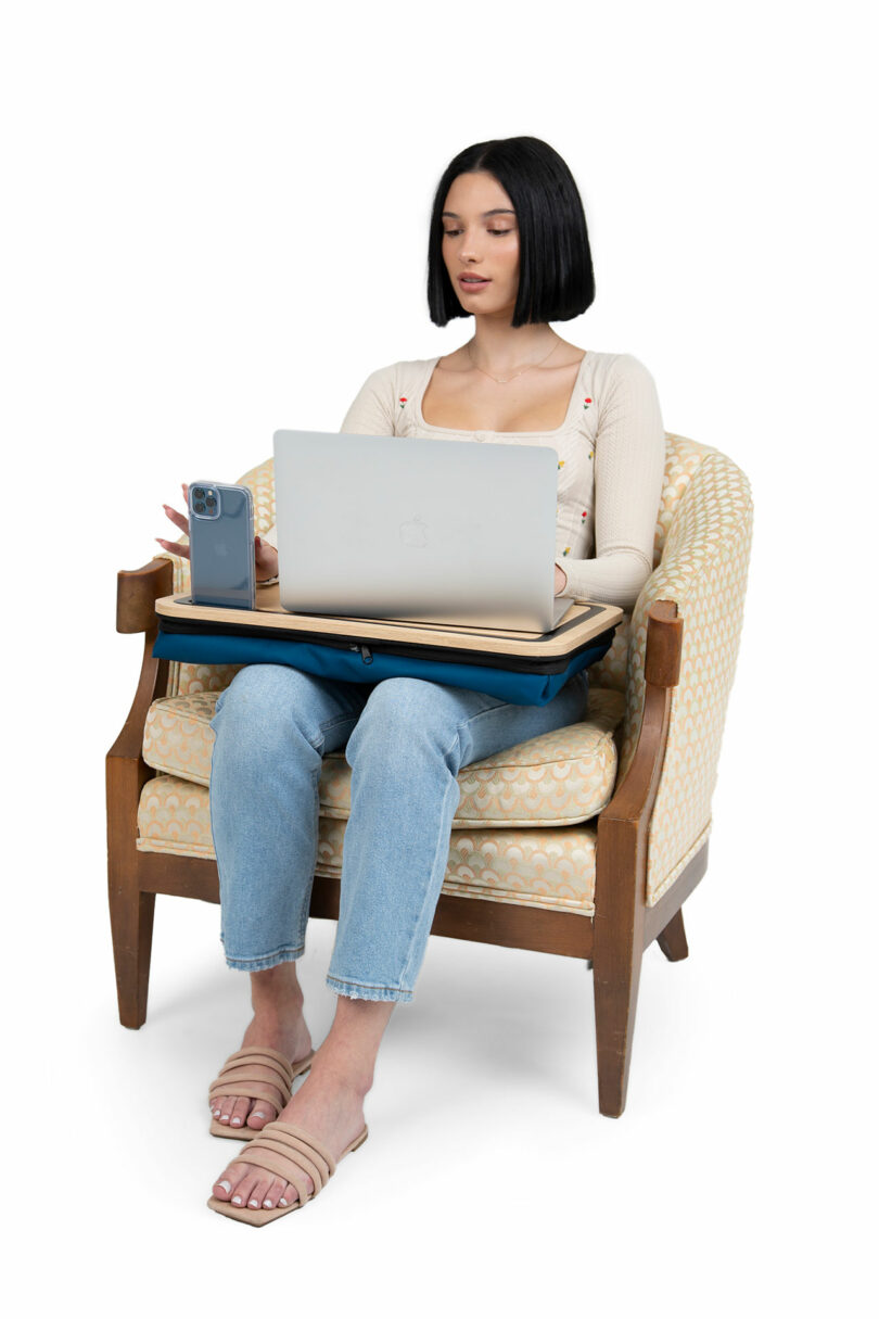 A woman sitting comfortably in a chair using a laptop on the Arlo Skye lap desk with an upright posture.