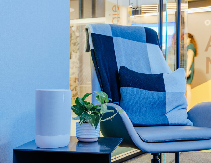 A cozy gray lounge chair with a blue checkered throw blanket and a small plant nearby.