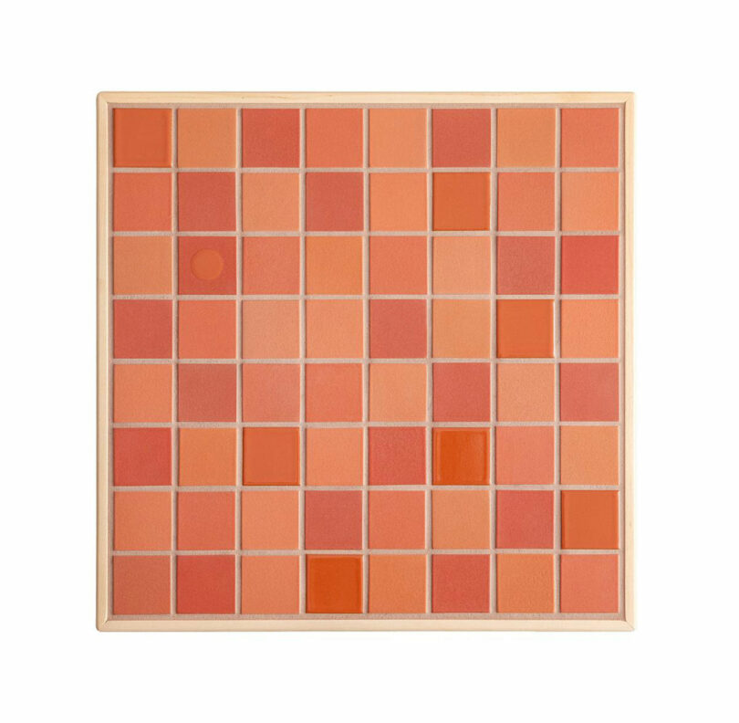 Close-up of variegated red and orange kiln-fired ceramic tiles within a wooden frame.