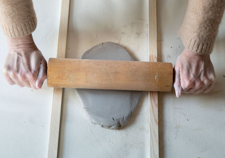 Hands rolling air-dry clay between two wooden guides to ensure even thickness.