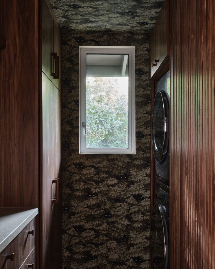 A laundry room detail featuring dark botanical wallpaper with hidden eye patterns and continued walnut paneling.