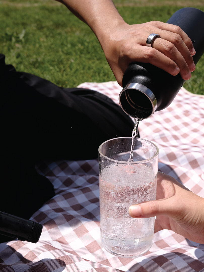 Two people on a picnic blanket sharing sparkling water poured from a black Aerflo-equipped bottle.
