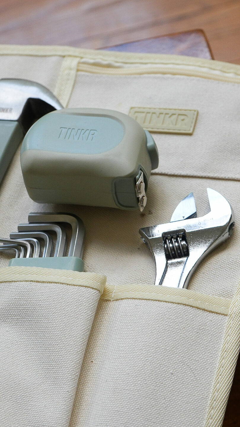 A branded TINKR tool pouch containing a tape measure, adjustable spanner, and hex keys.