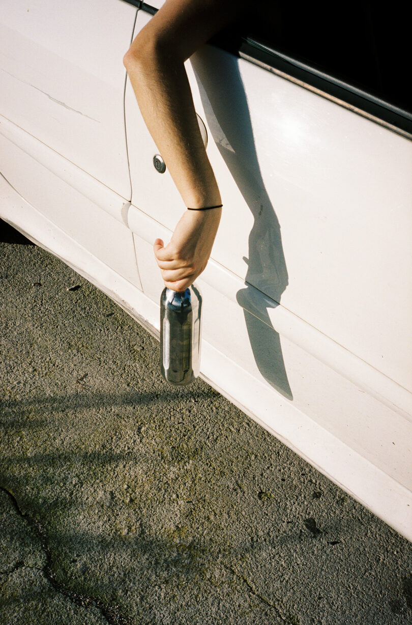 A hand holding an Aarke To-Go Bottle out of a car window against a sunny road backdrop.