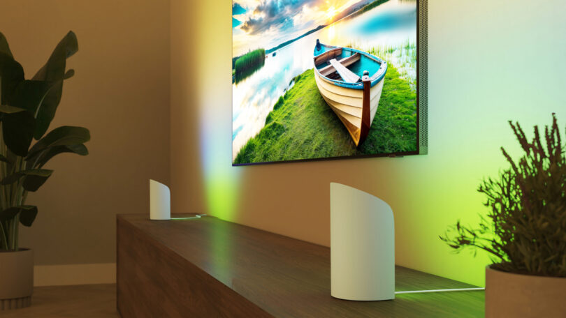 A living room featuring a wall-mounted TV with ambient lighting and two white Hue devices on a wooden console.