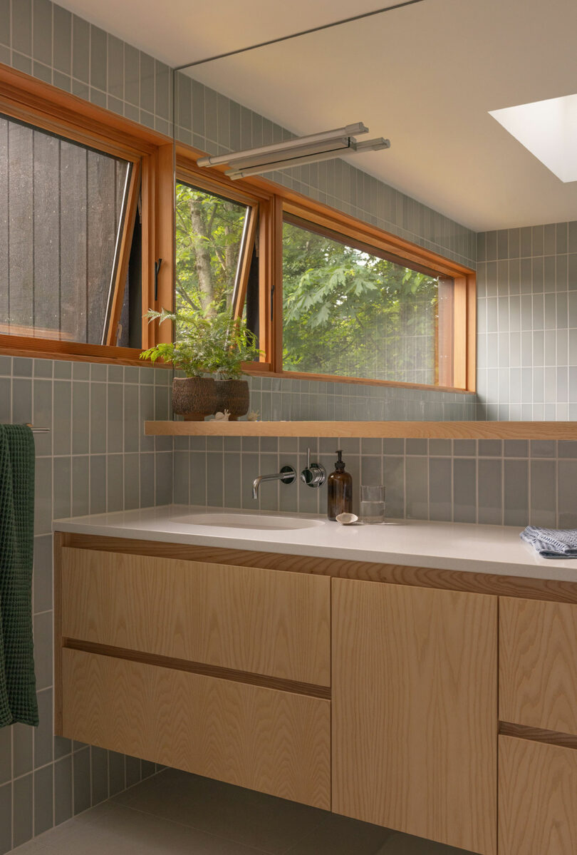 Modern bathroom featuring light-green vertical tiles, wooden vanity, and large windows.