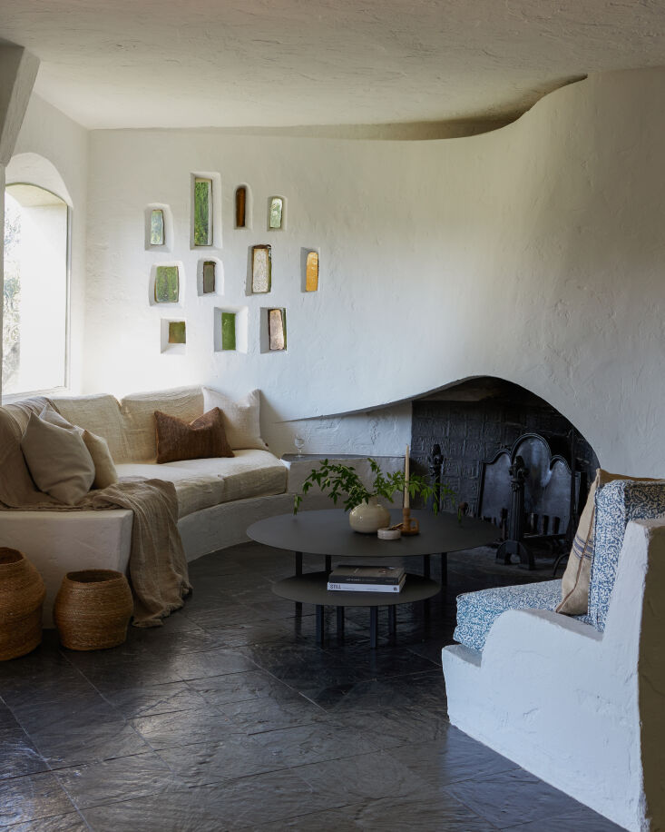 A white, rounded plaster built-in sofa with organic curves and linen throw cushions in a Mediterranean villa.