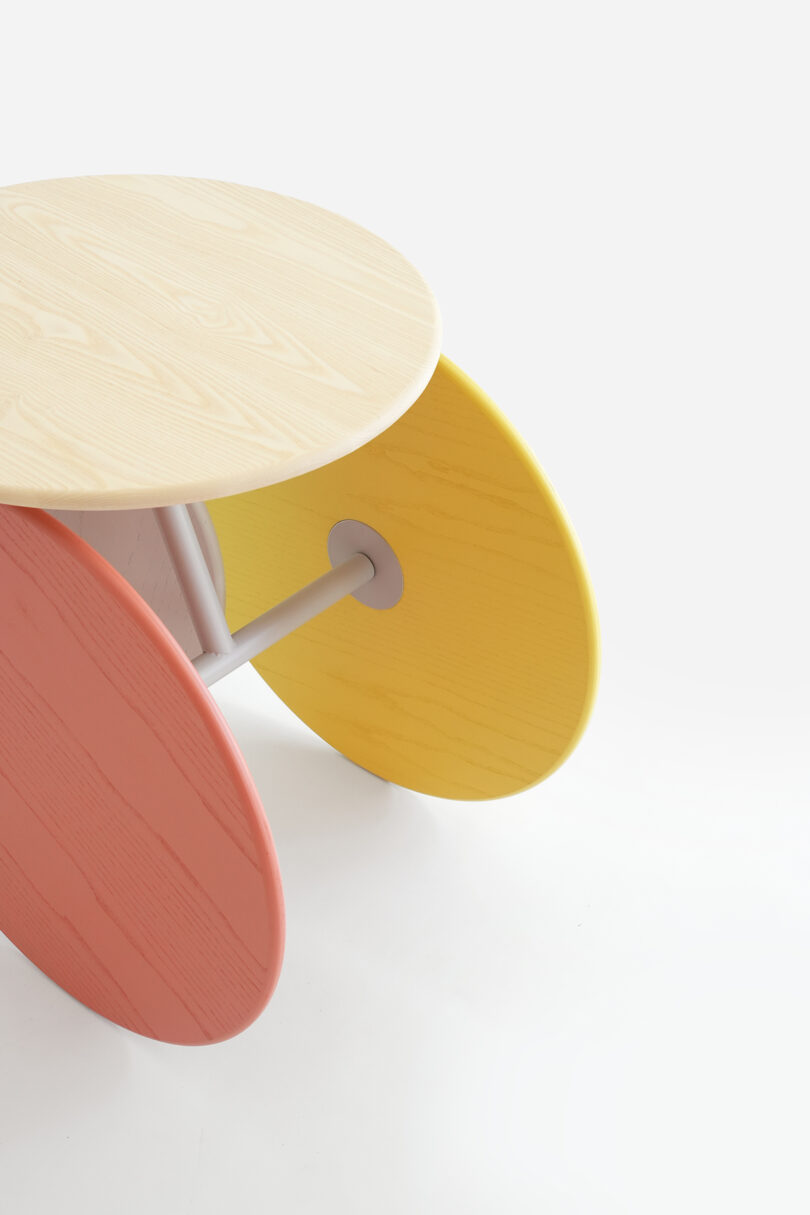 A modern table with colorful, angled oval-shaped legs in pink, yellow, and natural wood.