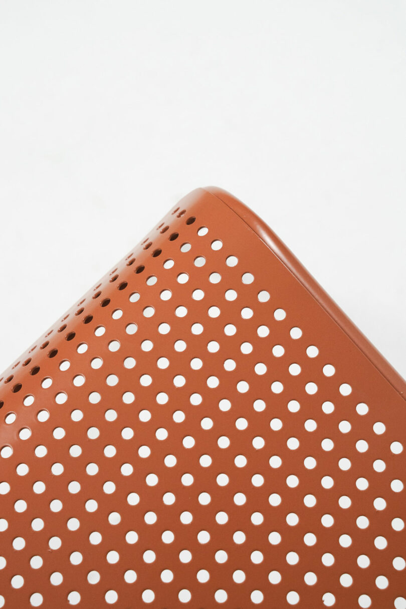 Macro close-up of circular CNC laser-cut perforations on a brown metal chair surface.