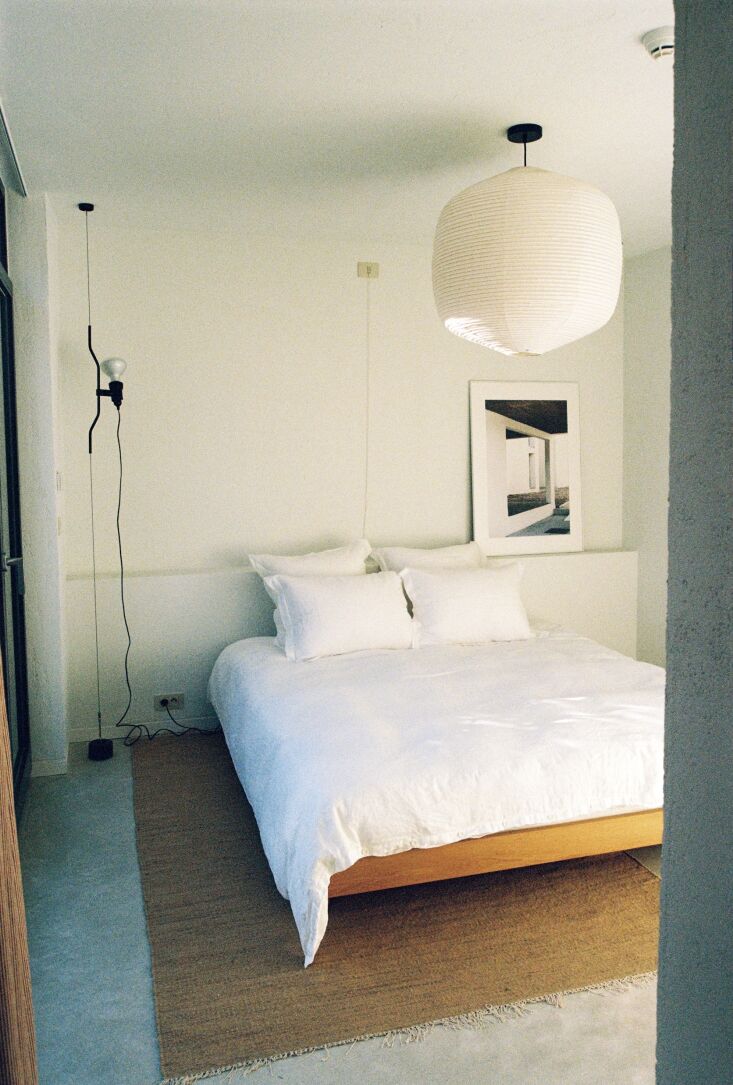 Bedroom with an oak bed frame, white Belgian linen bedding, and a suspended rice paper lantern.