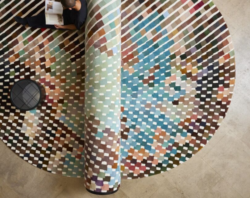 A person lying comfortably on a large modular bench-carpet while reading.
