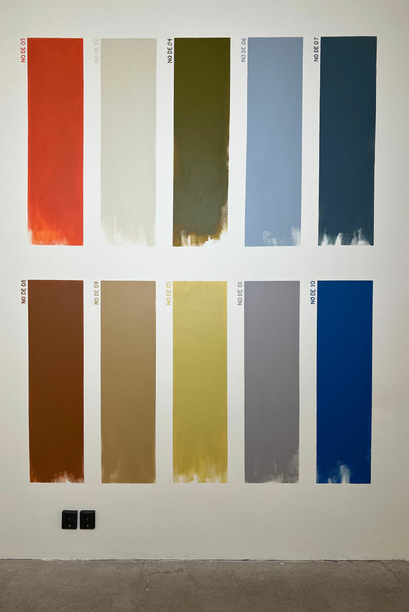 Ten rectangular paint swatches in varying tones of red, green, and blue displayed on a gallery wall.