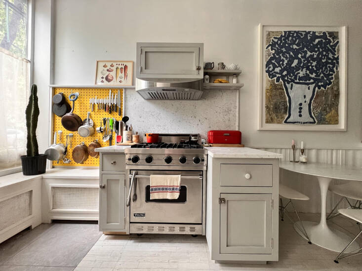 Wide view of a small kitchen with gray-white cabinets and a vibrant yellow pegboard backsplash.