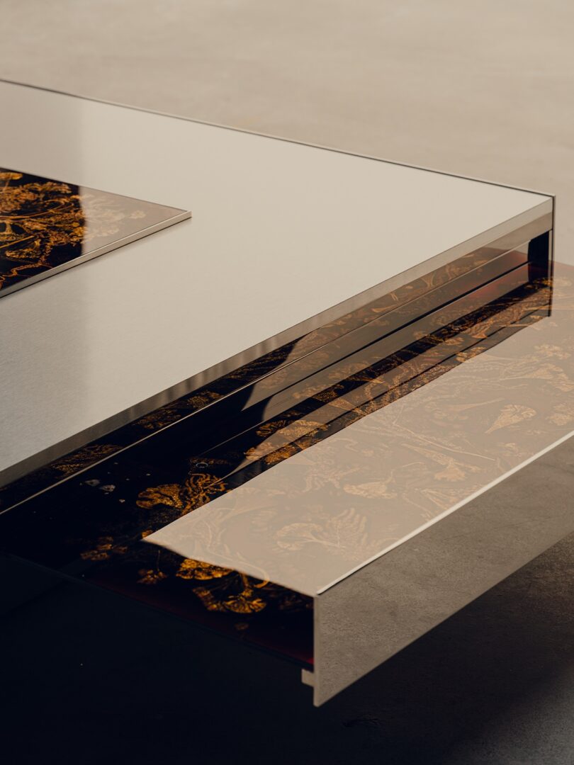 A modern coffee table with a reflective metallic frame and a decorative floral pattern visible through a transparent top.