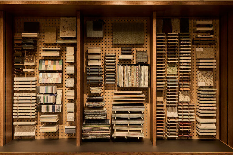 A close-up of wooden shelves neatly organized with various architectural material samples, fabrics, and tiles.