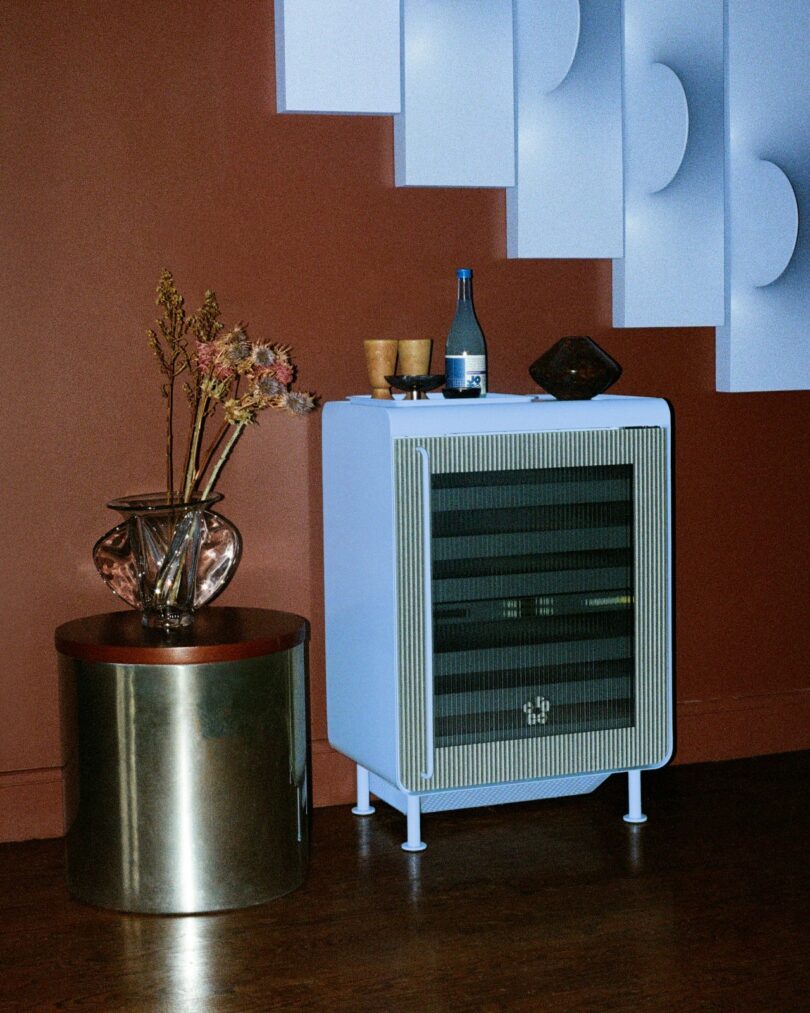 A white Rocco fridge used as a side table in a room with warm lighting and decorative flowers.