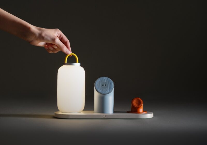 A hand lifting a portable white cylindrical lamp from a modular docking base with other magnetic components.