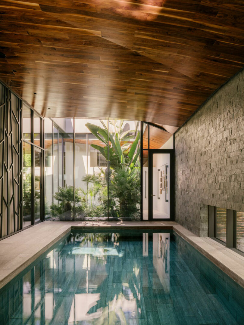 Modern indoor pool with sharp architectural lines, stone wall textures, and natural lighting from large windows.
