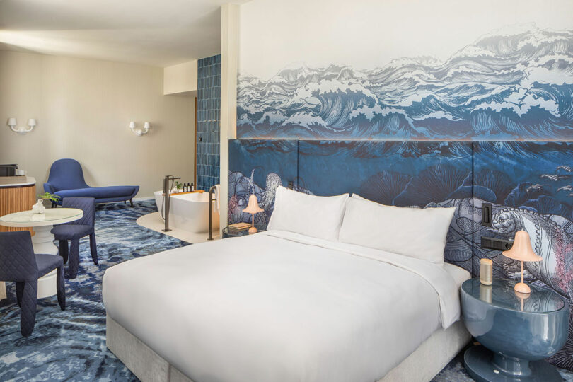 A premium hotel suite with blue accents, a large bed, and a freestanding bathtub.