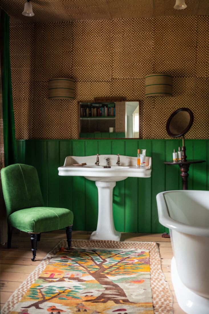 A guest bathroom in a centuries-old house featuring checked wallpaper, bright wainscotting, and layered vintage rugs.