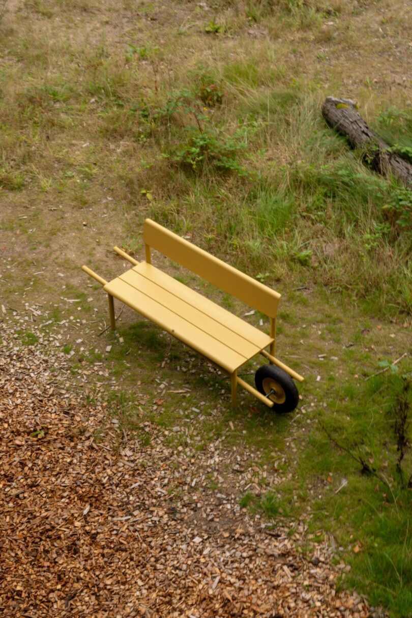 Profile view of a yellow aluminum bench with wheelbarrow-style handles and a single front wheel on grass.