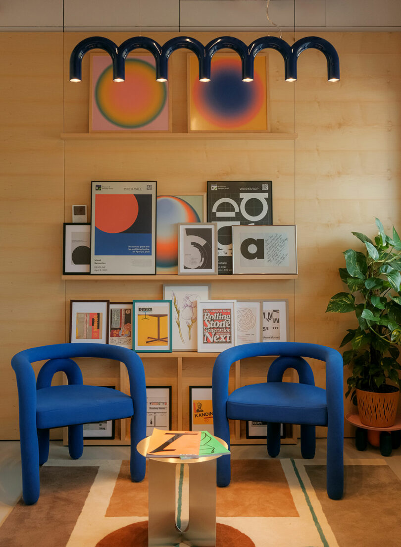 A gallery-style seating area with plush blue chairs, a low table, and abstract art on the wall.