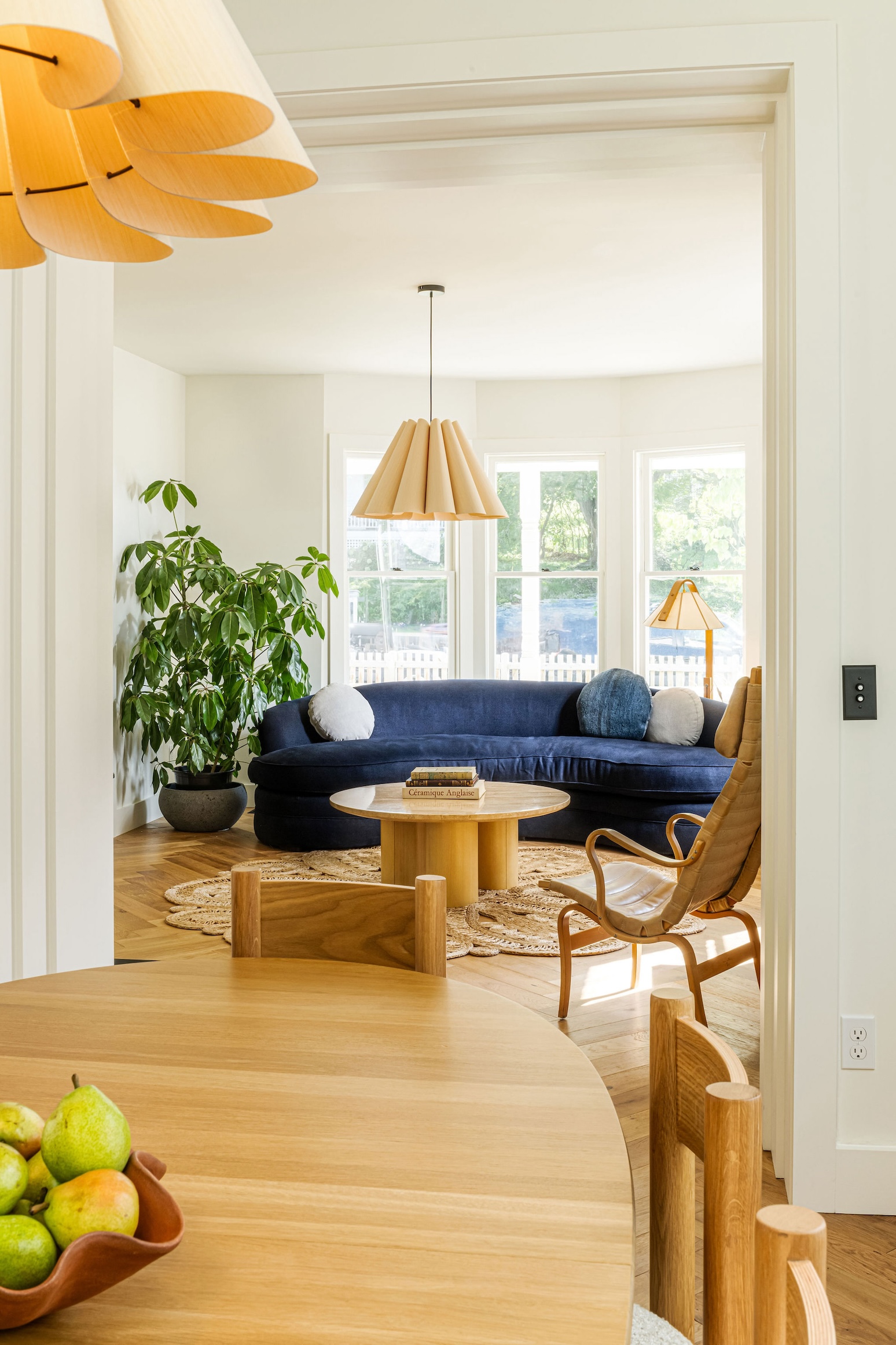 Living area featuring a curved vintage sofa in blue velvet and a Lora pendant light made of scalloped wood.