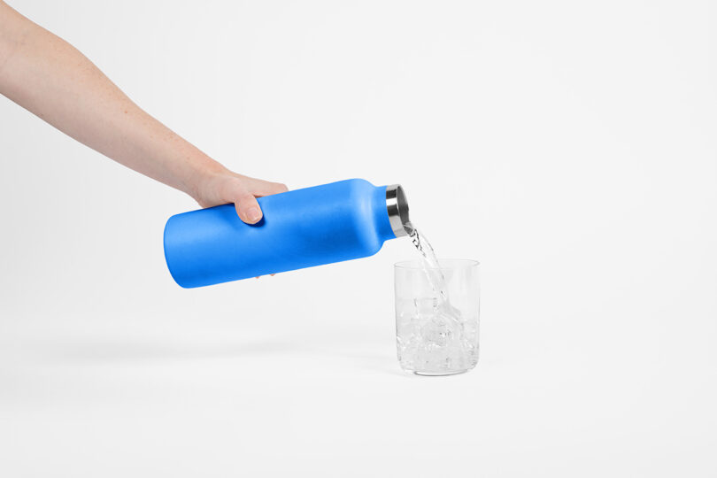 Chilled sparkling water being poured from a blue Hydro Flask into a glass filled with ice.