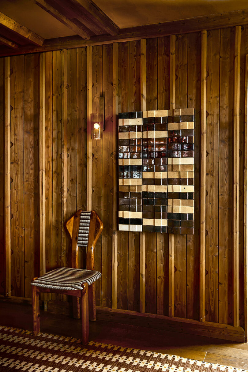 A close-up of a geometric wall art piece with brown and black tiles next to a striped wooden chair.